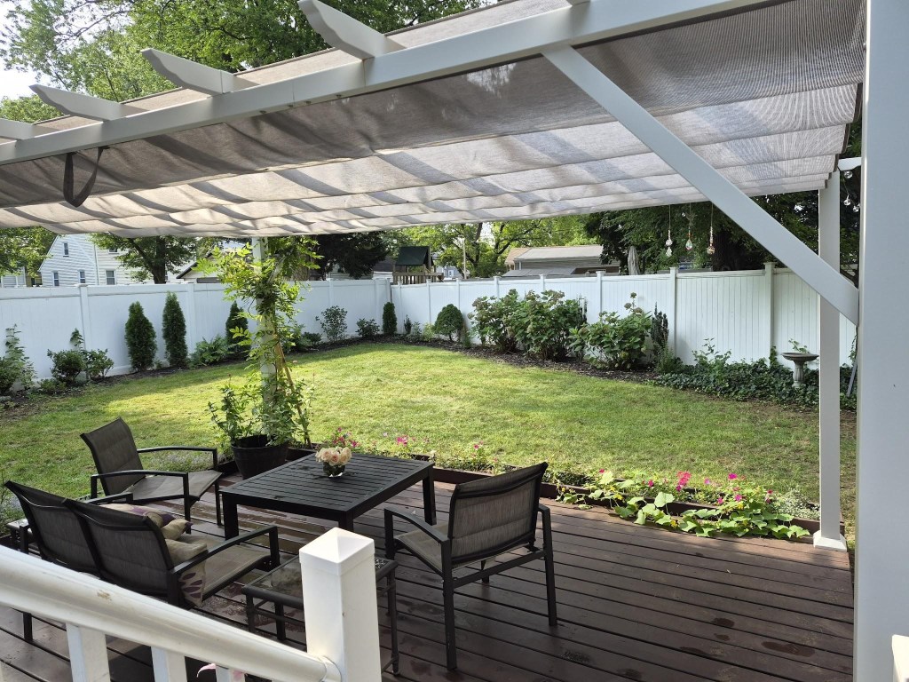 Finished white pergola with a gray retractable canopy shading the backyard deck and patio furniture.
