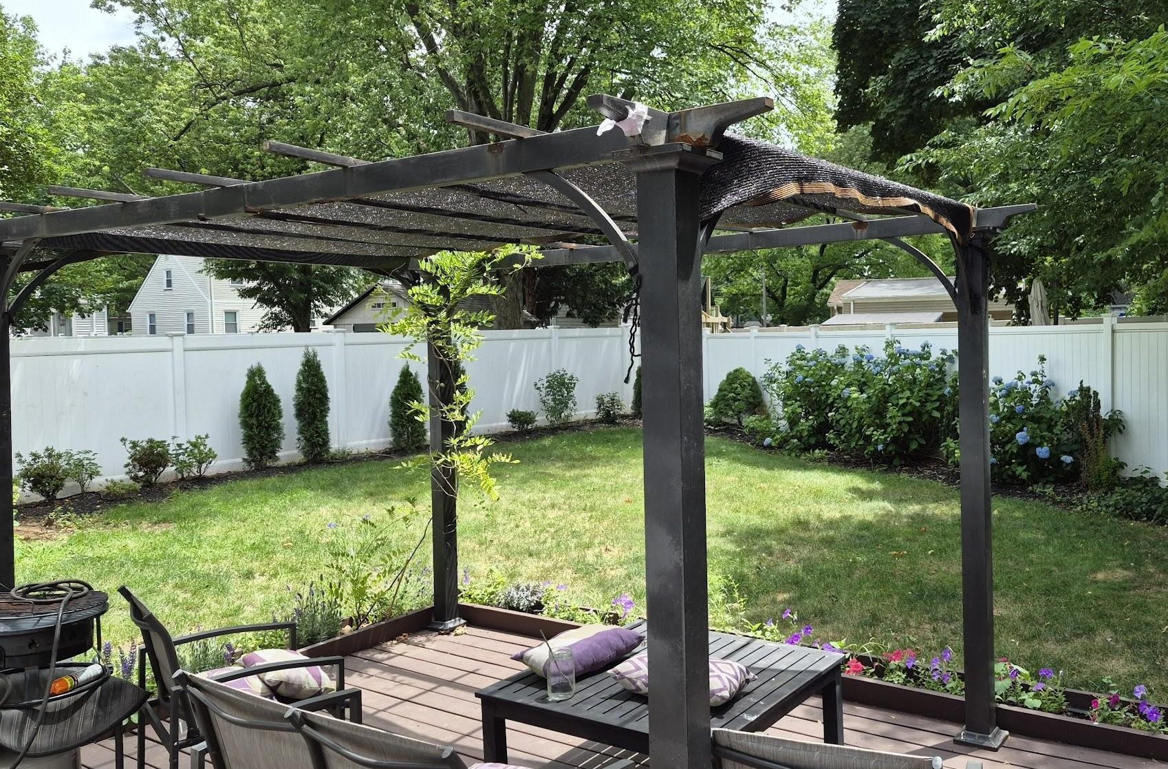 Old black aluminum pergola with a worn fabric canopy shading part of a backyard deck.

